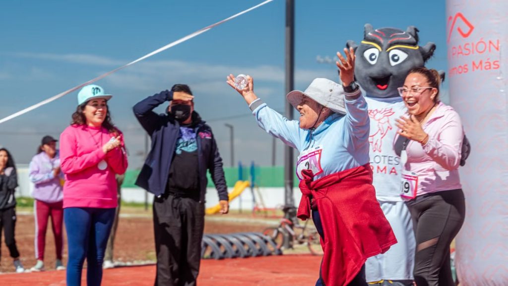 A senior woman joyfully crosses the finish line in a fun run event outdoors.